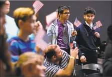  ?? Kin Man Hui / San Antonio Express-News ?? New, young American citizens wave flags after taking the Oath of Allegiance.