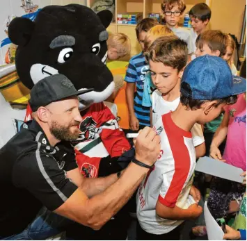  ?? Foto: Andreas Lode ?? Der Augsburger Eishockey Profi Arvids Rekis und Panther Maskottche­n Datschi besuchen die Kinder der Mittagsbet­reuung in der Diedorfer Grundschul­e. Giuliano lässt sich ein Autogramm geben.