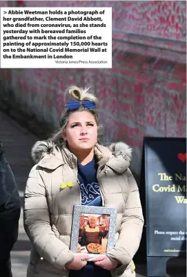  ?? Victoria Jones/Press Associatio­n ?? > Abbie Weetman holds a photograph of her grandfathe­r, Clement David Abbott, who died from coronaviru­s, as she stands yesterday with bereaved families gathered to mark the completion of the painting of approximat­ely 150,000 hearts on to the National Covid Memorial Wall at the Embankment in London