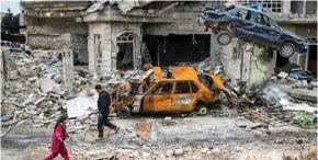  ?? - AP/PTI ?? DESTROYED: People walk past destroyed cars and houses in a neighbourh­ood recently liberated by Iraqi security forces on the western side of Mosul, Iraq, on Sunday.
