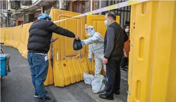  ?? — AFP photo ?? A worker, wearing a protective gear, guards the entrance to a neighbourh­ood in lockdown as a measure against the Covid-19 coronaviru­s receive food from a delivery man, in Shanghai’s Jing’an district.