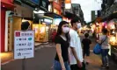  ??  ?? People walk past a sign reading ‘Wear protective face mask, wash your hands and keep social distancing’ at a night market in Taipei. Photograph: Ann Wang/Reuters