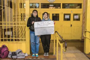  ?? SARAH PABST/THE NEW YORK TIMES ?? Agostina Fernandez Tirra, left, and Luana Pereyra, LGBTQ rights activists, hold a sign using gender-neutral language June 30 at their school in Buenos Aires, Argentina. The city bans gender-neutral language in schools.