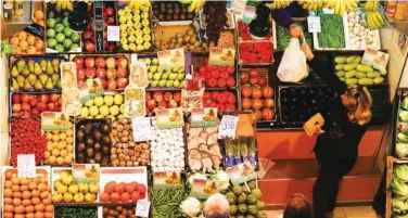  ?? R euters ?? ↑ A woman buys fruits and vegetables at a food market in Seville, Spain.