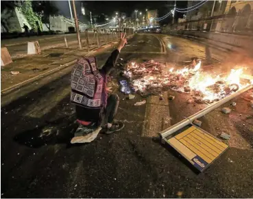  ?? /Reuters ?? Street rebel: A Palestinia­n sitting next to a burning barricade in Jerusalem, Israel, flashes a V-sign during clashes with Israeli police, as the Muslim holy fasting month of Ramadan continues.