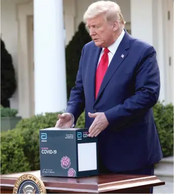  ?? WIN MCNAMEE/GETTY IMAGES ?? President Donald Trump holds a new COVID-19 test kit developed by Abbott Labs during the daily coronaviru­s briefing at the White House in late March.