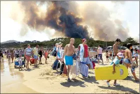  ?? AP/CLAUDE PARIS ?? Sunbathers and swimmers leave the beach at Le Lavandou on the French Riviera under an evacuation order Wednesday as smoke from a wildfire billows over the southern Cote d’Azur region. Large areas of Mediterran­ean forest have been burned after three...