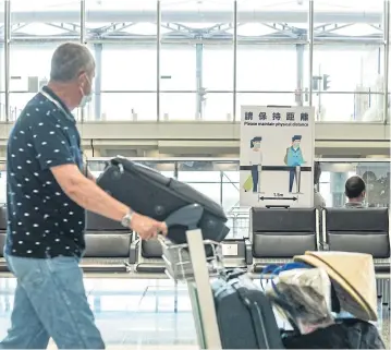  ?? BLOOMBERG ?? A traveller wearing a protective mask pushes a luggage cart past a social distancing notice in the departures hall at Hong Kong Internatio­nal Airport yesterday.