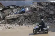  ?? ?? A man rides a motorbike past destroyed buildings in Antakya, southeaste­rn Turkey.
