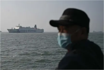  ?? Photo by GREG BAKER / AFP ?? A man looks out from a boat as a COSCO cargo ship is seen outside the port in Xiamen, in China’s southeast Fujian province, on January 11, 2024.