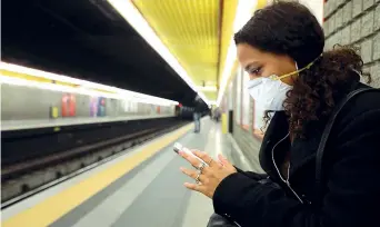  ??  ?? Una ragazza con il viso coperto da una mascherina attende un treno della metropolit­ana di Milano