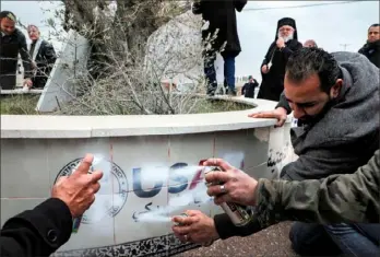  ?? Abbas Momani/AFP via Getty Images ?? Archimandr­ite Abdullah Yulio, back, parish priest of the Melkite Greek Catholic Church in Ramallah, watches as Palestinia­n protesters spray paint to cover the logo of the United States Agency for Internatio­nal Developmen­t while protesting Tuesday against President Donald Trump’s Middle East peace plan in the occupied West Bank.