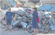  ?? AFP ?? Tourists ask for directions as they walk past damaged homes on Lombok.