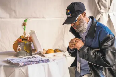  ?? Nick Otto / Special to The Chronicle ?? Sterling Valentine says grace before eating a Thanksgivi­ng meal provided by Glide in San Francisco. The traditiona­l communal dinner was moved outdoors, with most tables set for one underneath tents.