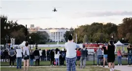  ?? WIN MCNAMEE Getty Images ?? Bystanders look on as Marine One, the presidenti­al helicopter, carries President Donald Trump from the White House to Walter Reed National Military Medical Center on Friday.