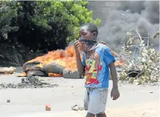  ?? /AFP Photo ?? Outbreak: A child covers his mouth in Lusaka’s Kanyama township as he walks past burning tyres on Friday.