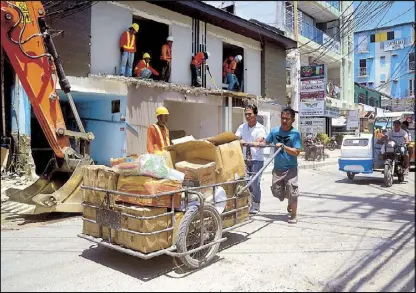  ??  ?? Workers demolish a store as villagers carry belongings while leaving the resort island of Boracay on Friday.