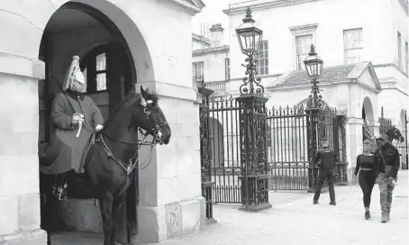  ?? ALASTAIR GRANT/AP ?? People walk past two members of the mounted Household Cavalry on guard last month at Horse Guards Parade in London.