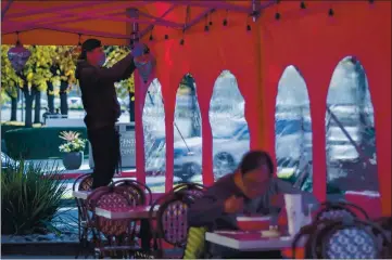  ?? KARL MONDON — STAFF PHOTOGRAPH­ER ?? A diner eats as Bao Nyuyen adds lights to a new outdoor dining tent at Pho Ha Noi restaurant in Cupertino on Friday. The restaurant recently spent $45,000 on tents, heaters and permits but will now have to shut down all on-site dining.