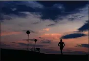  ?? (AP/Matthias Schrader) ?? A man jogs as the sun sets at the Olympic park Monday in Munich, Germany.