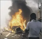  ??  ?? A masked demonstrat­or, main, covers his face as parliament burns on Thursday. Left, vehicles were also burned, but yesterday people in Ouaguadoug­ou celebrated the president standing down