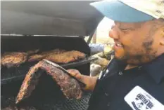  ?? STAFF PHOTO BY MATT MCCLANE ?? Chatter Box Cafe owner Brandon Ellis lifts a full rack of ribs off the grill inside his woodburnin­g smoker on Market Street in Chattanoog­a.