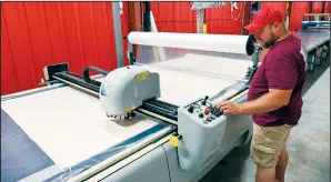  ??  ?? Kevin Holzman, cutting technician, programs the cutting machine to cut the white fabric used to make the American flag at North American Manufactur­ing on June 28 in Scranton.