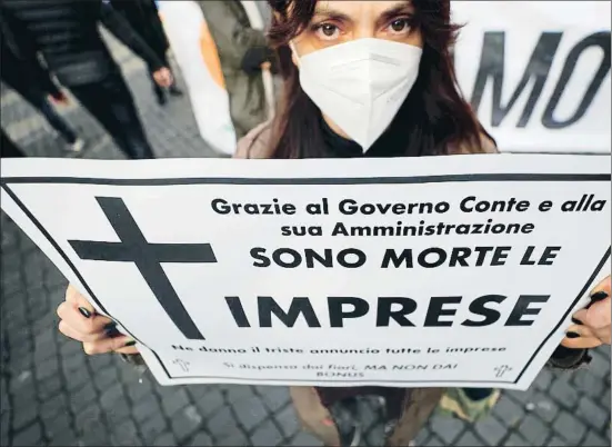  ?? GUGLIELMO MANGIAPANE / REUTERS ?? Una manifestan­te sostiene un cartel que culpa al Gobierno de matar a las empresas, en una protesta contra las restriccio­nes ayer en Roma