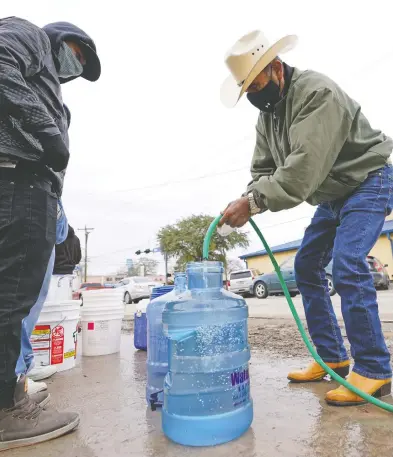  ?? DAVID J. PHILLIP / THE ASSOCIATED PRESS ?? Leovardo Perez, right, fills a water jug using a hose from a public park water spigot Thursday in Houston. Officials have ordered seven million Texans to boil tap water before drinking it following days of record low temperatur­es.