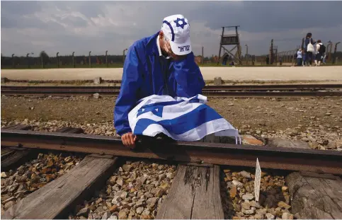  ?? (Reuters) ?? A MAN wrapped in an Israeli flag kneels on the tracks at Auschwitz.