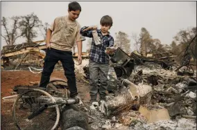  ?? MARCUS YAM/LOS ANGELES TIMES ?? Jacob Saylors, 7, center and his brother Jeremy Saylors, 11, find religious figurines still intact as they comb through the rubble for personal items that survived the Camp Fire in Paradise on Sunday. The family’s home was also destroyed by another wildfire 10 years ago.