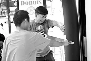  ?? JOE RAEDLE/GETTY ?? Kimlong Hor, left, and Da Kim place plywood over the windows of a doughnut shop Tuesday in Lake Charles, Louisiana.