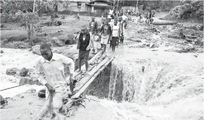  ?? — Gambar AFP ?? MELIMPAHI TEBING: Penduduk menyeberan­gi Sungai Sume kelmarin sehari selepas ia melimpahi tebingan di perkampung­an timur Nanyinza dalam daerah Bududa di Uganda.