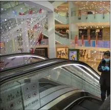  ?? MARK SCHIEFELBE­IN - STAFF, AP ?? A woman wearing a face mask and gloves rides an escalator at a mostly empty shopping mall in Beijing. With the COVID-19 disease spreading in the U.S., it could deal a major blow to the country’s malls.