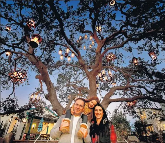  ?? Photograph­s courtesy of Rancho Mission Viejo ?? RESIDENTS MATT and Amy Fuccile, with daughter Charlie, bask in the glow of one of Rancho Mission Viejo’s three chandelier trees, a project of Adam Tenenbaum. The trees canopy a communal table in the Esencia village of the master-planned community.