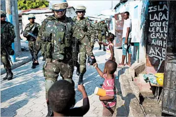  ?? DIEU NALIO CHERY/AP ?? U.N. peacekeepe­rs from Brazil fist-bump with children as they patrol in the Cite Soleil slum, near Port-au-Prince, Haiti.