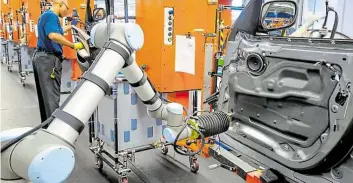  ?? DPA-BILD: ROLLISON ?? Moderne Fertigung: Ein Roboter und ein Arbeiter arbeiten in der Produktion im BMW-Werk an einem neuen Auto.