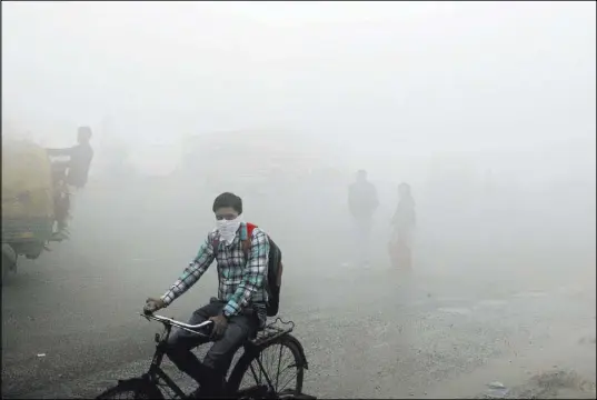  ?? Altaf Qadri The Associated Press ?? Commuters wait for transport amid a thick blanket of smog Friday on the outskirts of New Delhi, India. Air pollution peaked this week in the city, rising to more than 30 times the World Health Organizati­on’s recommende­d safe level.