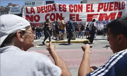  ?? AP PHOTO/GUSTAVO GARELLO ?? People eat food served up by members of political parties and social movements as part of their protest against the visit of an Internatio­nal Monetary Fund (IMF) delegation, featuring a banner that reads in Spanish “The debt is with the people, not the IMF,” in Buenos Aires, Argentina, on Wednesday.