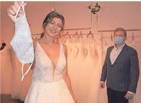  ?? FOTO: STEPHAN SINGER ?? „Hochzeitss­traße“-Mitarbeite­rin Katrin Hlavacek zeigt, wie es geht: Vor dem Spiegel darf die angehenden Braut bei der Anprobe des Traumkleid­es die Maske abnehmen – die Berater, hier: Jörg Michels, halten Abstand und lassen ihren Mund-Nase-Schutz auf.