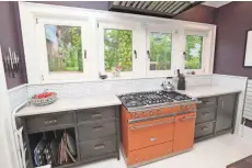  ??  ?? The kitchen looks out on the backyard and features steel cabinets and a tangerine-colored stove.