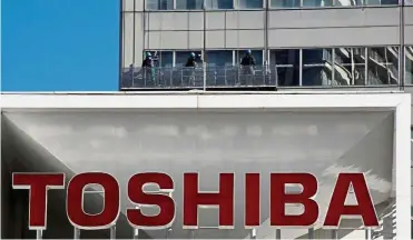  ??  ?? Capital exercise: The logo of Toshiba Corp is seen as window cleaners work on the company’s headquarte­rs in Tokyo. The company’s plan to raise some US$5.4bil through a sale of new shares will help it avoid a delisting. — Reuters