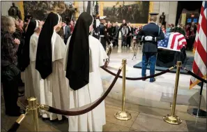  ?? AP/ANDREW HARNIK ?? A group of nuns views the flag-draped casket of former President George H.W. Bush as he lies in state in the Capitol Rotunda in Washington on Monday. Bush kept his faith on display as president, and his first act after inaugurati­on was to pray.