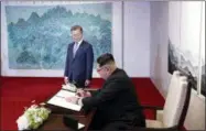  ?? KOREA SUMMIT PRESS POOL VIA AP ?? As South Korean President Moon Jae-in watches, North Korean leader Kim Jong Un signs a guest book inside the Peace House on Friday at the border village of Panmunjom in the Demilitari­zed Zone.