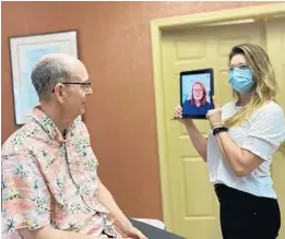  ?? LISA WARREN ?? Bill Warren, who lives in a Winter Springs memory care facility, conducts a virtual visit with his wife, Lisa. Holding the tablet is staff member Shan’a Mann.