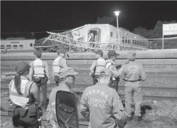  ??  ?? Taiwan search and rescue team officials wait for a crane to arrive at the crash site after the Puyuma Express train derailed at high speed near Xima station in northeaste­rn Yilan county Sunday killing at least 18 people. AGENCE FRANCE PRESSE