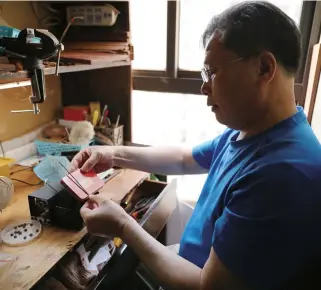  ??  ?? Xu Wenlong at work in his 1-square-meter workshop with a variety of tools piled on his bench — All photos by Zhu Gaoyi