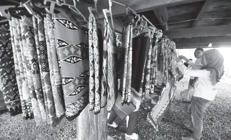  ??  ?? A WOMAN inspects the Maranao cloths and other crafts being sold at the tribal village inside Magsaysay Park. BING GONZALES