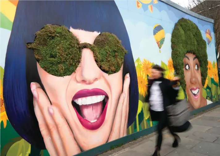  ?? ?? A pedestrian walks past a 'Green Living Wall' art project produced in collaborat­ion with The National Portrait Gallery and the Earls Court Developmen­t Company, at the former Earls Court Exhibition Centre site in London, Wednesday, Jan. 11, 2023. Demolished in 2016, the site is set to be redevelope­d. Photo: Associated Press.