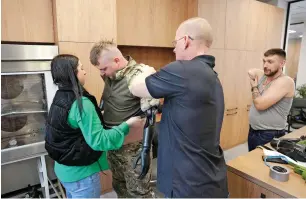  ?? — AFP ?? Veronika Kucherenko, the wife of Valery Kucherenko, together with upper limbs prosthetis­t James Allan, help Valeriy get dressed in the workshop of the Protez Foundation on April 2, 2024.